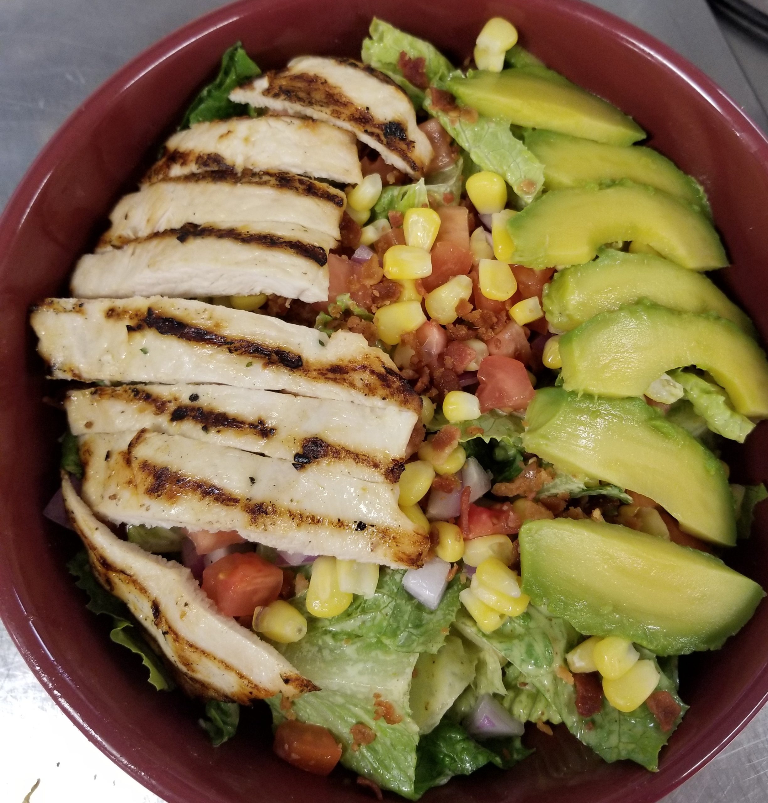 A bowl of chicken salad with avocado, corn and tomatoes.