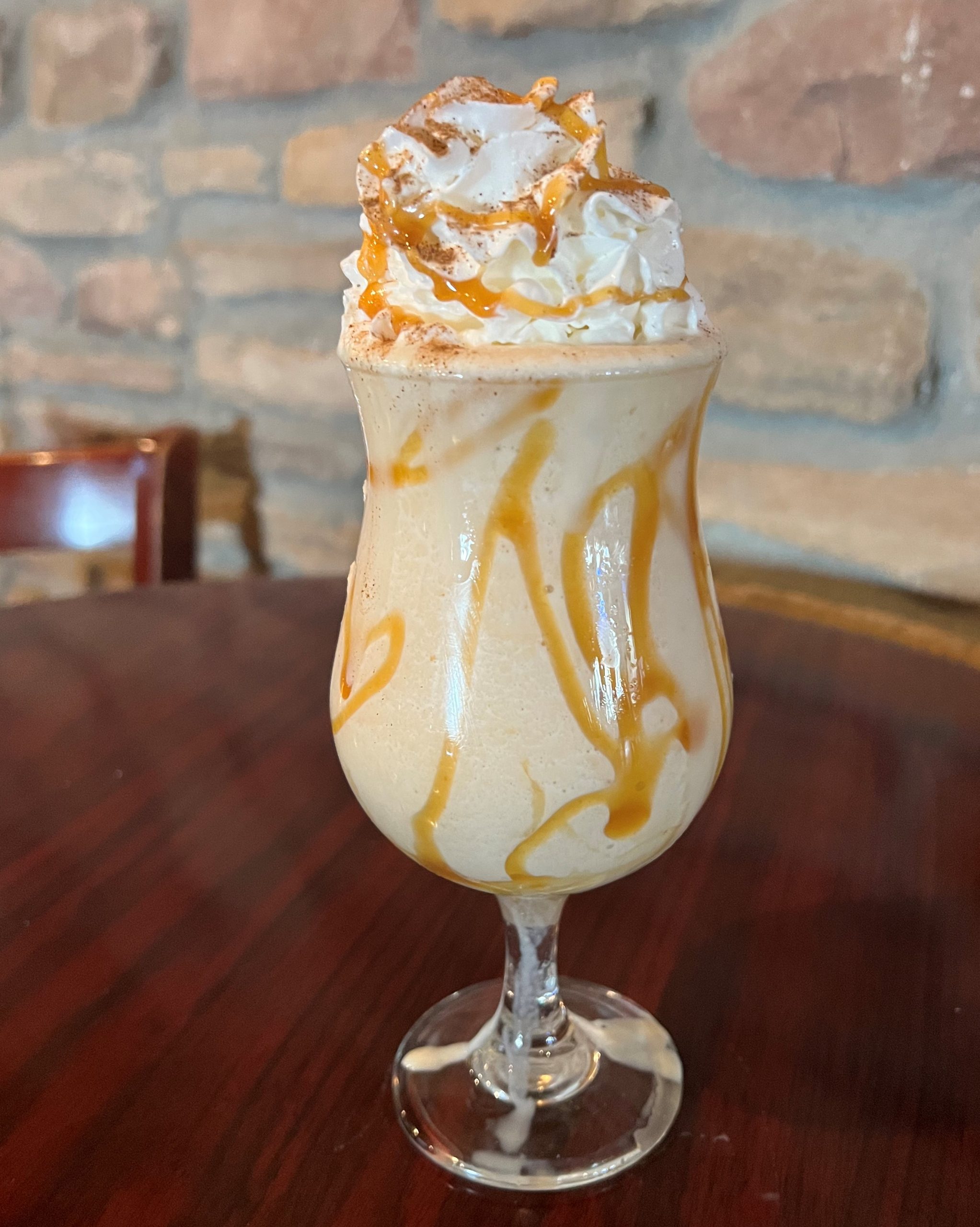 A margarita with caramel and whipped cream sitting on top of a wooden table.