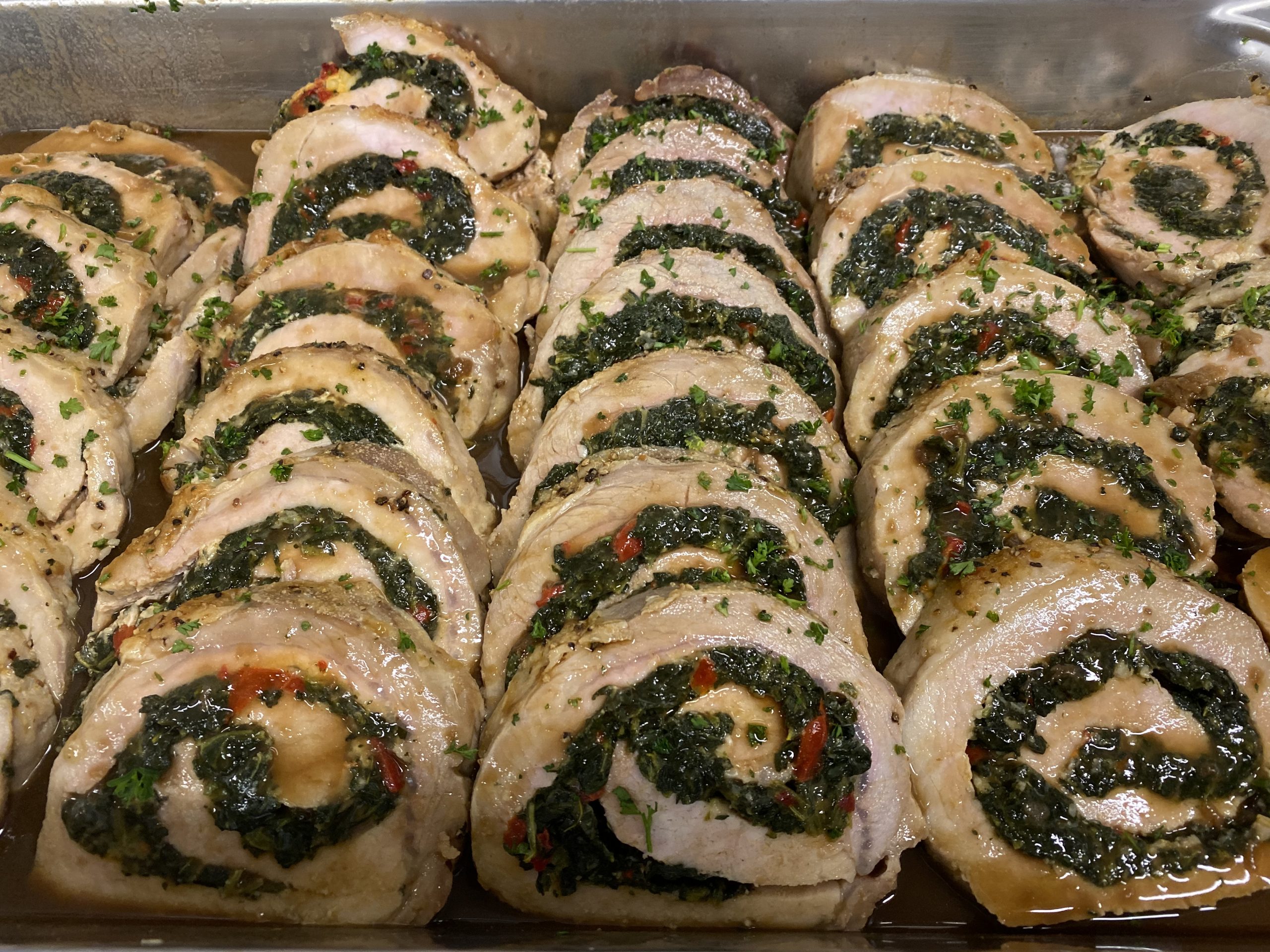 A tray of stuffed pork rolls with spinach and herbs.